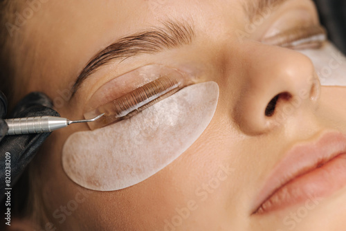 Close-up of eyelash care treatment procedures. Beautiful female, blond hair model have eyelashes lamination. Woman doing staining, curling, laminating and extension for lashes