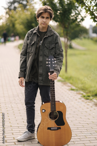 Concentrated teenage boy musician playing acoustic guitar outdoor. Handsome boy love music. Open your eyes. Focus on face