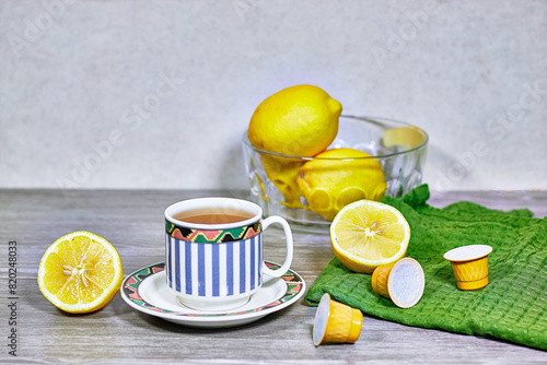 Glass cup with lemon, mint tisane  with with tea capsule on wood table 