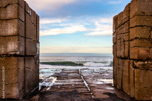 View of the sea at dawn, framed by two walls, breaking against a breakwater.