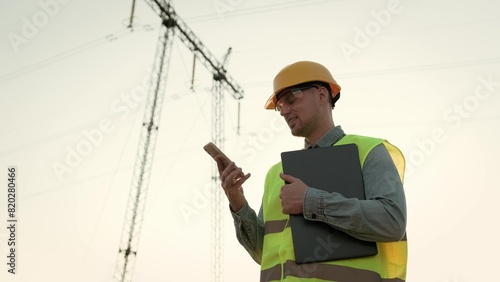 Joyous power line inspector communicating on cellphone near transmission tower