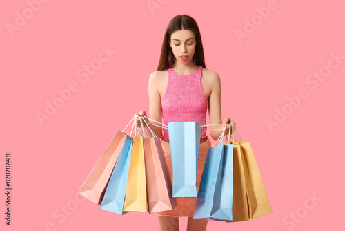 Beautiful young woman with shopping bags on pink background