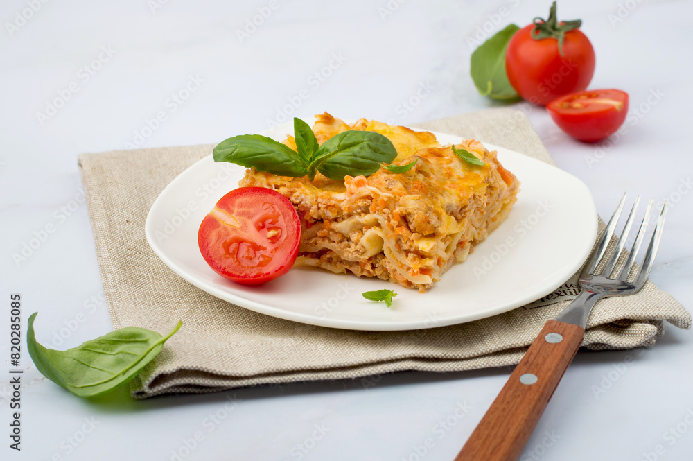Traditional Italian dish of lasagna with bolognese sauce garnished with basil and tomatoes on a white plate. Horizontal.. Traditional Italian dish of lasagna with bolognese sauce garnished with basil and tomatoes on a white plate. Horizontal..