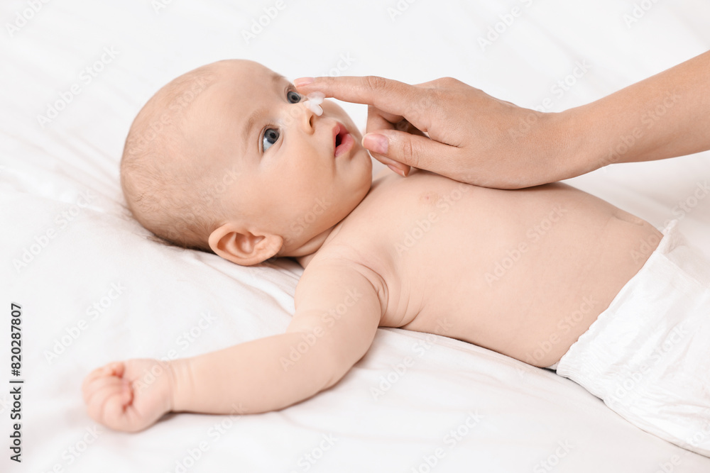 Woman applying cream onto baby`s face on bed, closeup Woman applying cream onto baby`s face on bed, closeup