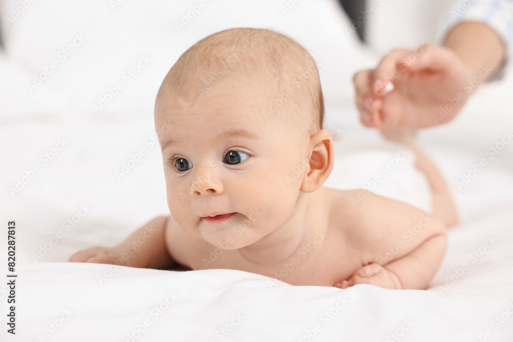 Woman applying body cream onto baby`s skin on bed, closeup Woman applying body cream onto baby`s skin on bed, closeup