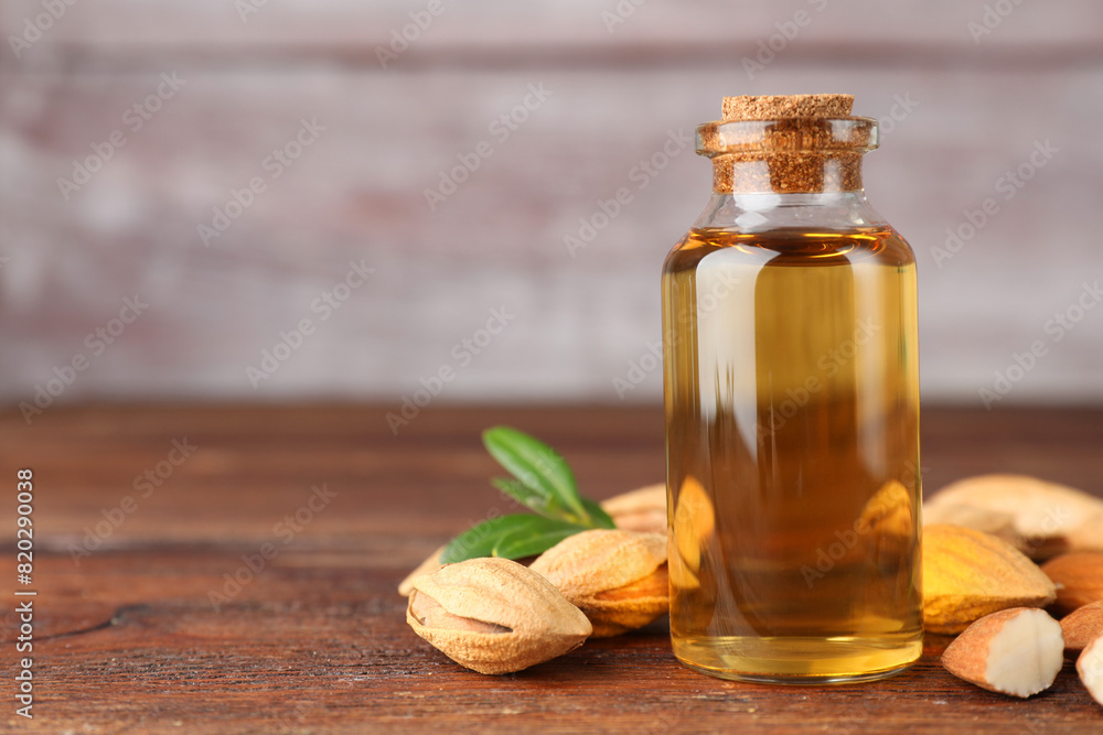 Almond oil in bottle, nuts and leaves on wooden table, closeup. Space for text Almond oil in bottle, nuts and leaves on wooden table, closeup. Space for text