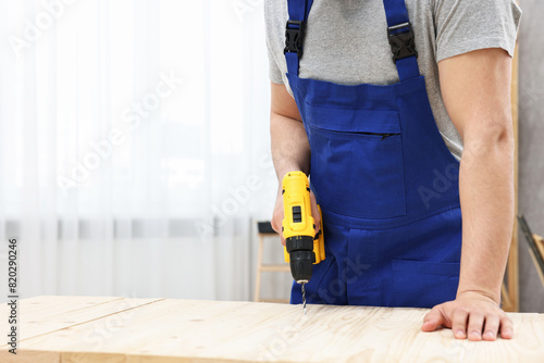 Young worker using electric drill at table in workshop, closeup