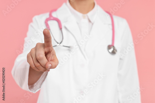 Doctor with stethoscope pointing on pink background, closeup
