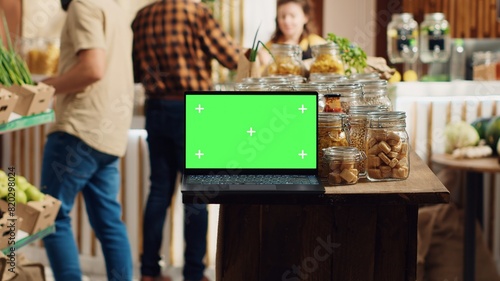 Chroma key laptop with copy space used as commercial sign in sustainable local shop. Promotional ad on green screen device in food store with products in reusable glass jar package photo