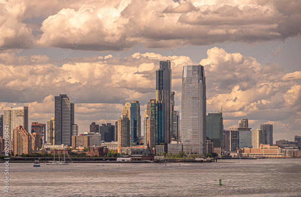 New York, NY, USA - August 1, 2023: Skyscraper buildings of New Jersey city along the Hudson river waterfront under blue-gray cloudscape