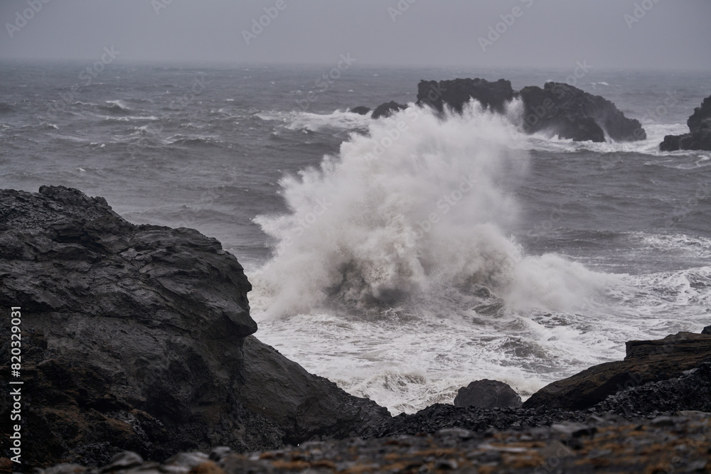 Two waves collide with each other on the coast of Iceland with view of basalt rocks