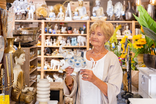 Focused mature woman looking for decorative statue at household store