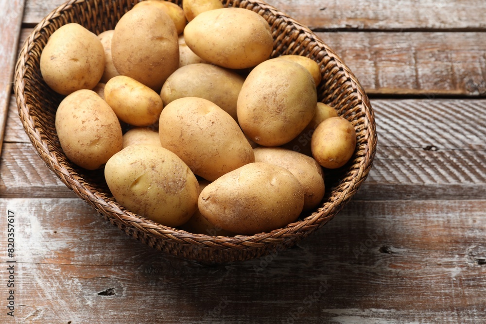 Raw fresh potatoes in wicker basket on wooden table Raw fresh potatoes in wicker basket on wooden table
