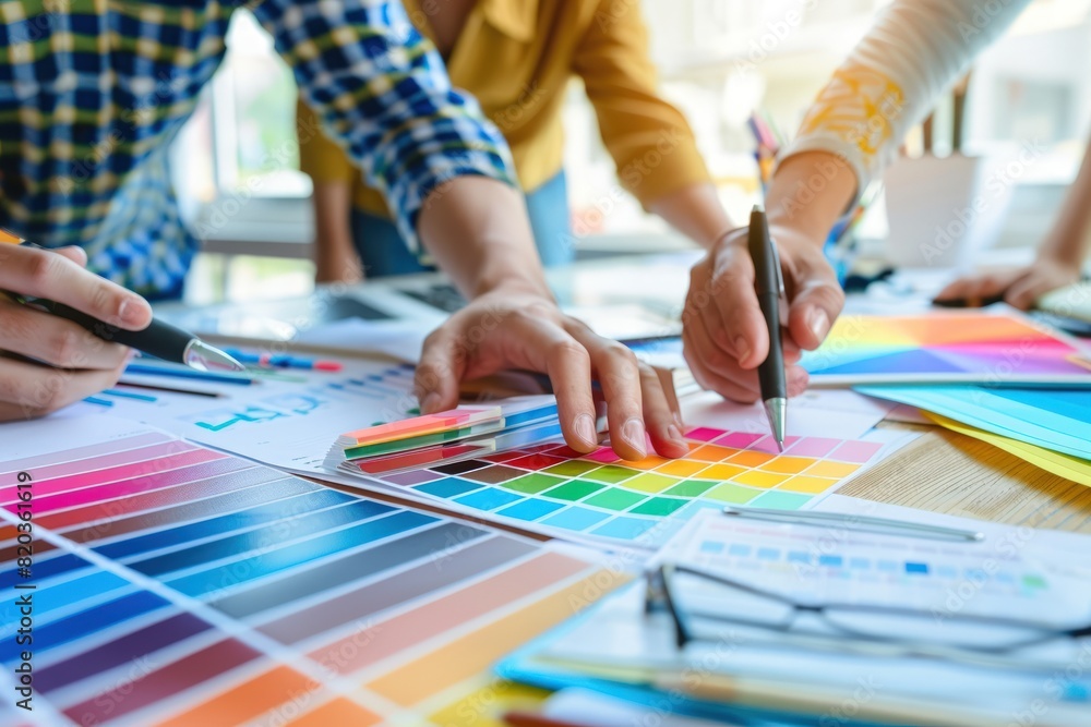 Fototapeta premium Business people are discussing a marketing plan while pointing at color swatches and graphs on a table in their office.