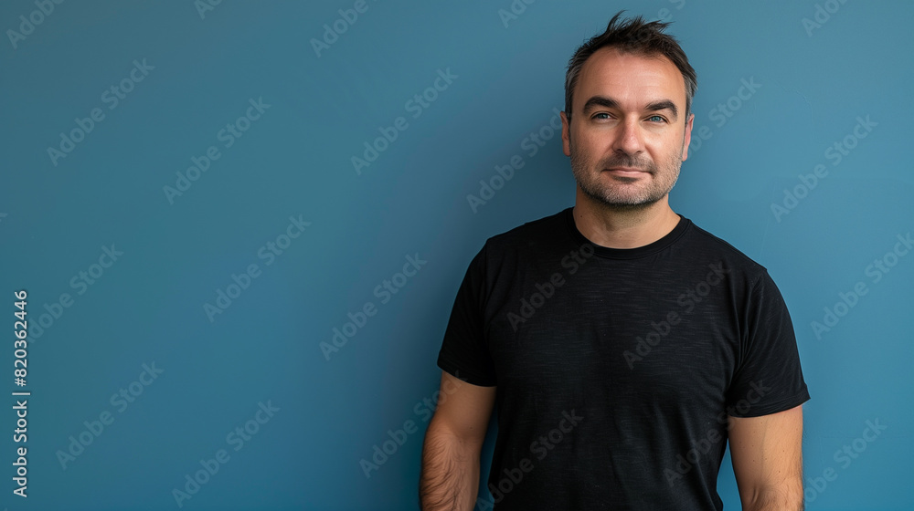 portrait of a man in black shirt standing against blue wall portrait of a man in black shirt standing against blue wall