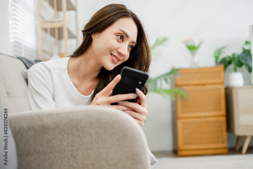 A woman is sitting on a couch and looking at her cell phone. She is smiling and she is enjoying herself A woman is sitting on a couch and looking at her cell phone. She is smiling and she is enjoying herself