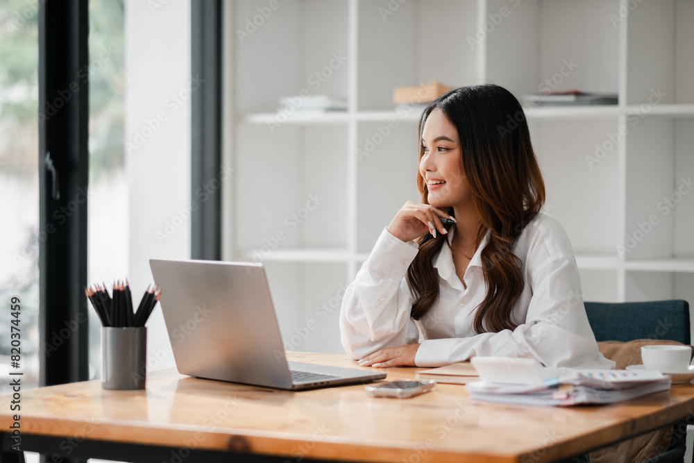 A woman is sitting at a desk with a laptop and a cell phone. She is smiling and she is enjoying her work A woman is sitting at a desk with a laptop and a cell phone. She is smiling and she is enjoying her work