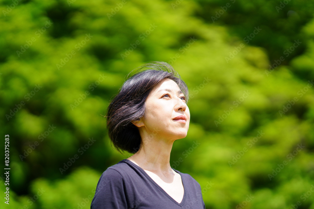 緑の中で日差しを浴びて立つ中年女性 緑の中で日差しを浴びて立つ中年女性