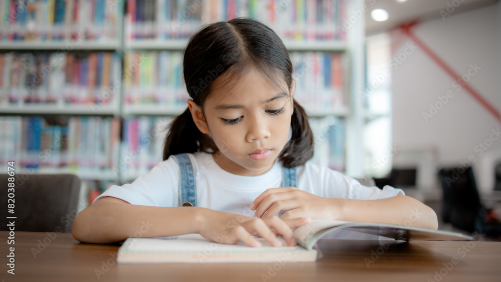 A young girl is sitting at a table in a library, reading a book A young girl is sitting at a table in a library, reading a book