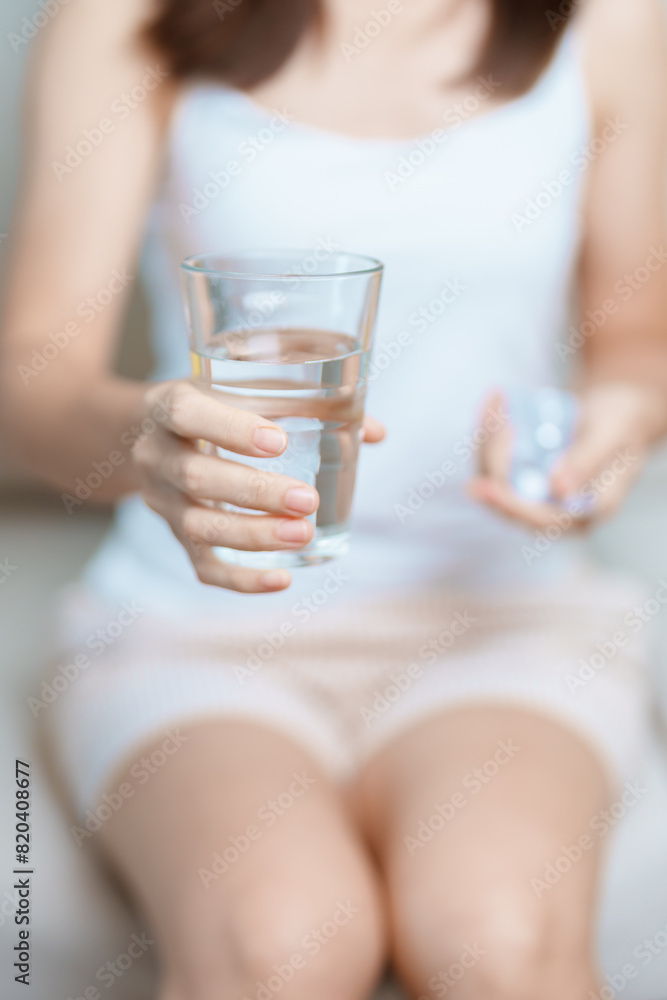 woman hand holding medicine painkiller pill and water glass on the sofa at home, taking for headaches, stomach ache, Diarrhea Pain from food poisoning, Endometriosis, Hysterectomy and Menstrual woman hand holding medicine painkiller pill and water glass on the sofa at home, taking for headaches, stomach ache, Diarrhea Pain from food poisoning, Endometriosis, Hysterectomy and Menstrual