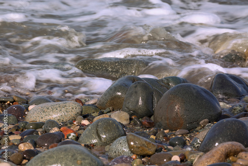 A wave runs over wet pebbles. The water's edge. Close-up