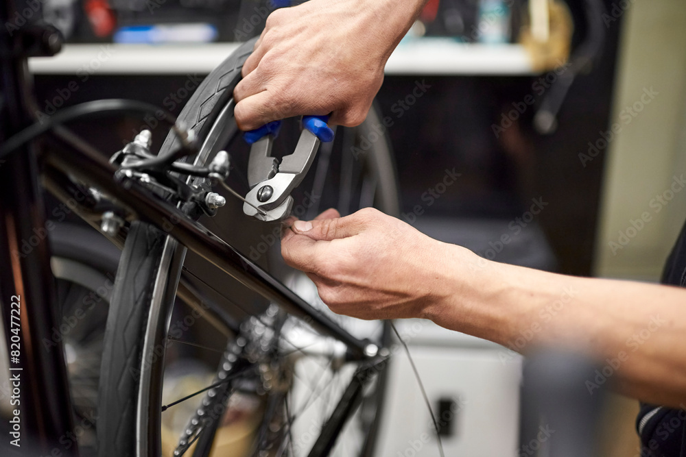 Fototapeta premium Unknown repairman cutting a bicycle wire with a cable cutter tool in his repair shop. Close up composition with selective focus and copy space. Real people at work.