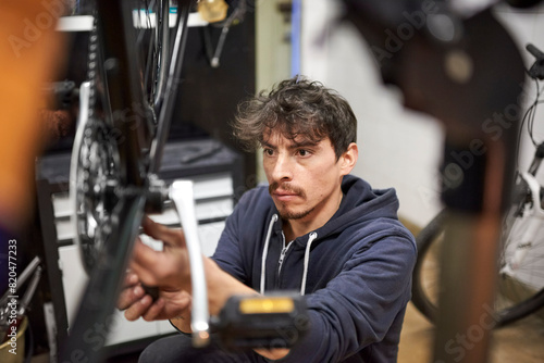 Portrait of an hispanic man focused assembling a bicycle in his bike shop as part of a maintenance service. Composition with the subject framed and selective focus. Real people at work.
