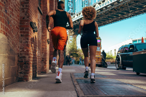 A man and a woman jogging under the Brooklyn bridge