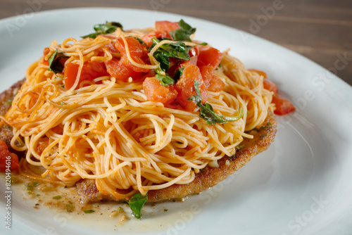 A closeup view of a dish featuring angel hair pasta and breaded chicken cutlets.