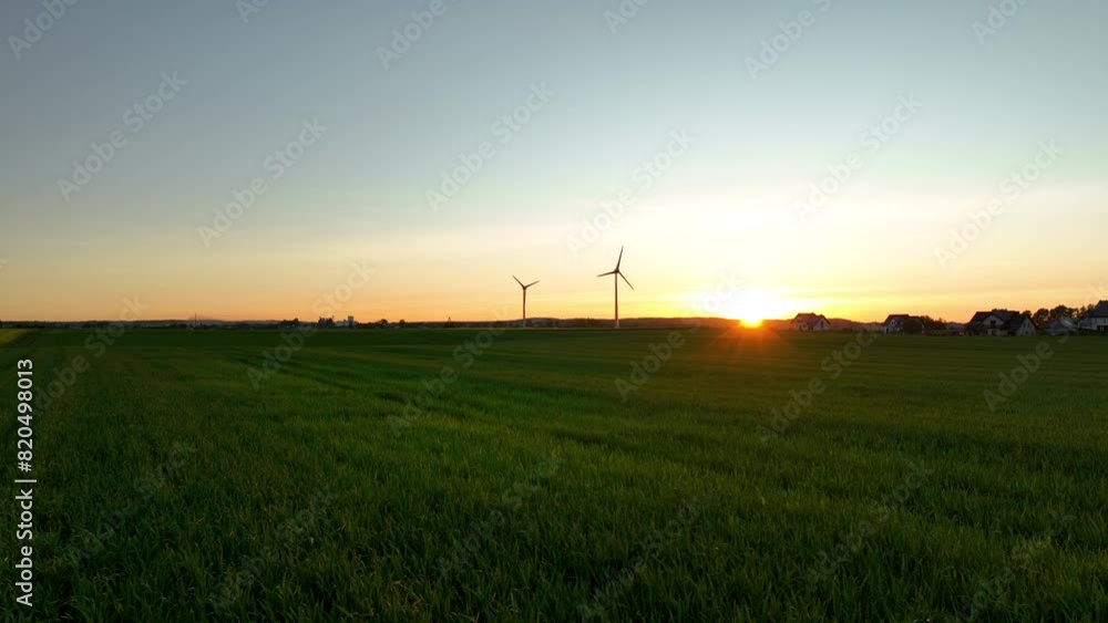Expansive green fields with wind turbines at sunset, distant houses, golden light, tranquil.