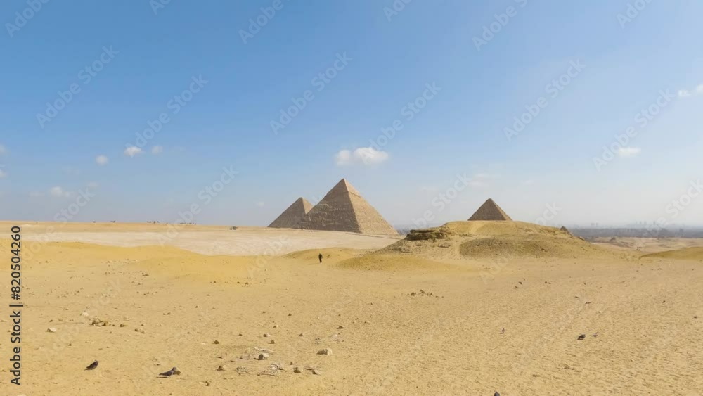 Rolling desert dunes with Great Pyramids of Giza in distance under blue sky of Egypt Rolling desert dunes with Great Pyramids of Giza in distance under blue sky of Egypt
