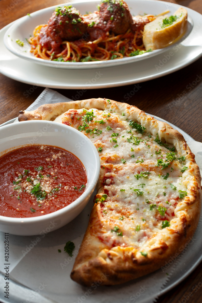 A view of a calzone entree, with a side of marinara dipping sauce. A view of a calzone entree, with a side of marinara dipping sauce.