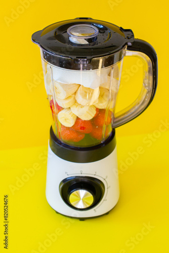 White mixer with fruits and berries, banana, strawberry on yellow background photo