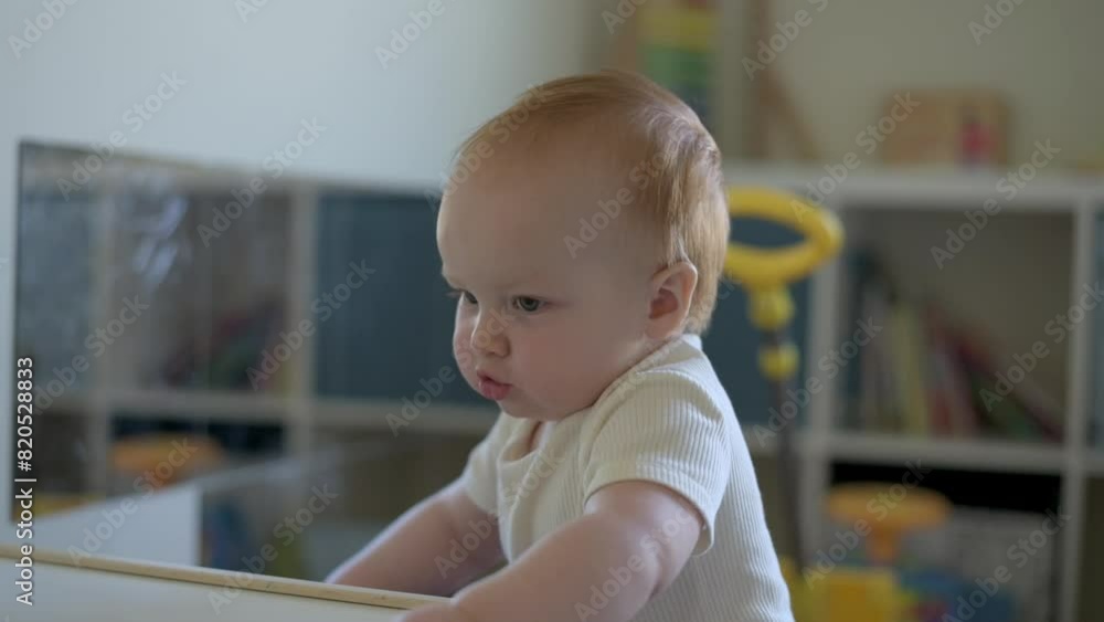 A charming toddler smiles warmly while leaning on a white table in a well-equipped playroom, surrounded by toys, embodying the joy and curiosity of early childhood. A charming toddler smiles warmly while leaning on a white table in a well-equipped playroom, surrounded by toys, embodying the joy and curiosity of early childhood.
