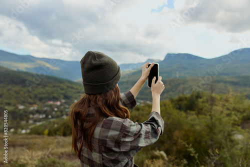 A woman capturing a breathtaking view of the majestic mountain range on her smartphone during a scenic travel adventure