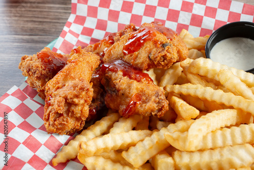 A closeup view of a basket of deep fried chicken wings with a side of crinkle cut french fries.