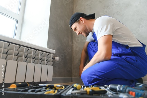 Cheerful male worker, plumber checking pipes while installing heating system in apartment photo