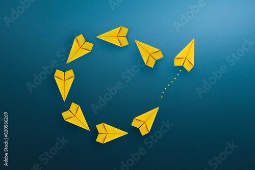 Group of yellow paper planes float in a circular direction and one paper plane pointing in different way. Business concept for new ideas creativity and innovative solution.