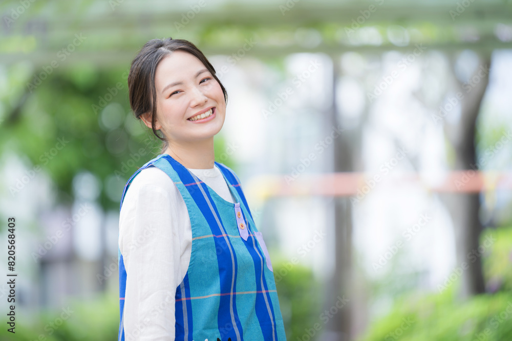 園庭でカメラ目線のエプロンを着た保育士のイメージ　コピースぺースあり