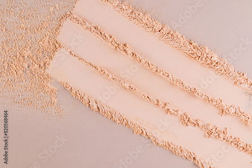Three parallel stripes of a delicate texture of decorative face powder in a natural tone on a beige background. View from above. Swatch powder.