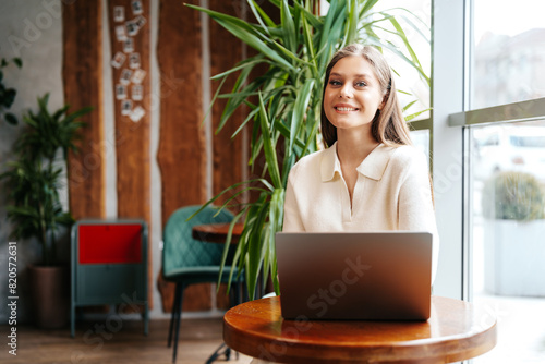 Smiling Young Woman Working on Laptop at Cozy Cafe During Daytime © fotofabrika