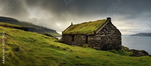 shabby stone walls and straw roof located on green grassy hill under blue cloudy sky photo