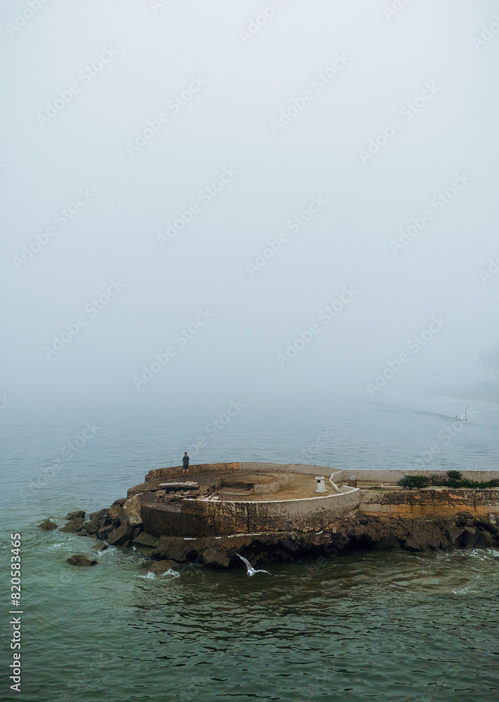 A cloudy day in Mazatlan shows a man fishing from a pier. The sea is calm, and a gray sky looms overhead, creating a serene yet moody atmosphere. A cloudy day in Mazatlan shows a man fishing from a pier. The sea is calm, and a gray sky looms overhead, creating a serene yet moody atmosphere.