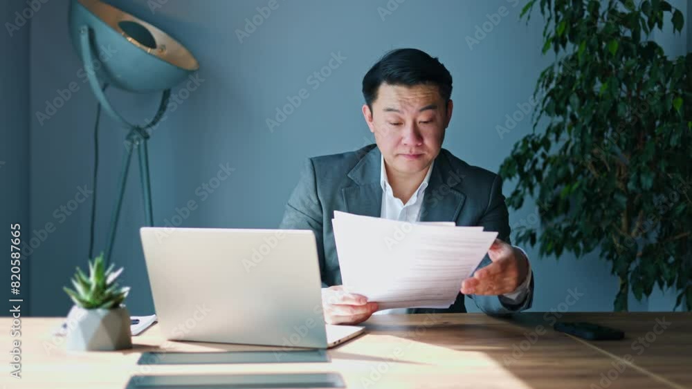 Tired japanese entrepreneur falling asleep while reading boring documents during work process in sunny cabinet. Hardworking male boss reviewing paper reports and preparing business project indoors. Tired japanese entrepreneur falling asleep while reading boring documents during work process in sunny cabinet. Hardworking male boss reviewing paper reports and preparing business project indoors.