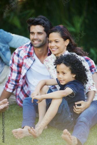 Smile, nature and child with parents in park bonding together on outdoor family vacation. Happy, love and boy kid with mother and father relaxing on grass in garden for countryside holiday or trip.