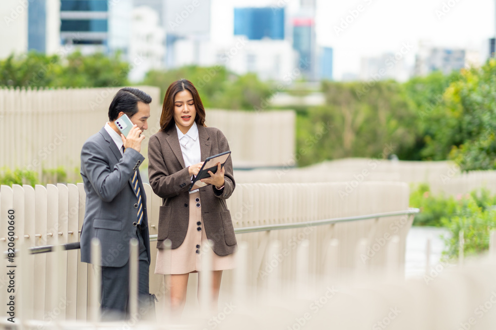 Asian businessman and woman working on digital tablet for new business project together in the city. Business people colleague teamwork meeting discussion corporate business together outside office.