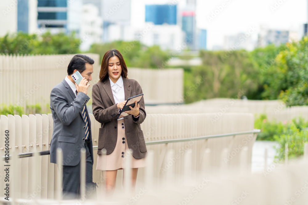 Fototapeta premium Asian businessman and woman working on digital tablet for new business project together in the city. Business people colleague teamwork meeting discussion corporate business together outside office.