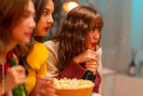 Group of Young Asian woman friends watching movie on television together in living room at home at night. Generation z girl enjoy and fun indoor lifestyle meeting party on summer holiday vacation.