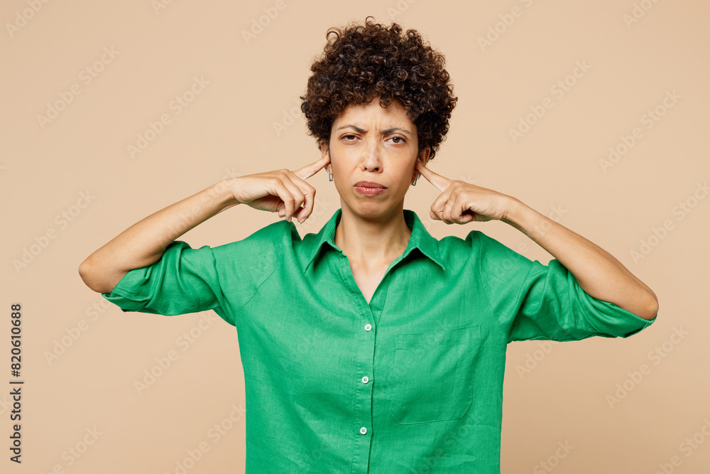Young sad woman of African American ethnicity in green shirt casual clothes cover ears with hands fingers do not want listen scream isolated on plain pastel beige background studio Lifestyle concept Young sad woman of African American ethnicity in green shirt casual clothes cover ears with hands fingers do not want listen scream isolated on plain pastel beige background studio Lifestyle concept