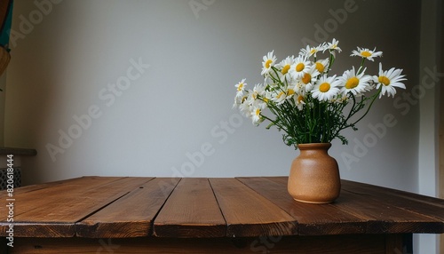 Rustic Charm: Wooden Table with Beige Clay Vase of Chamomile Flowers Against a Blank White Wall © Sadaqat